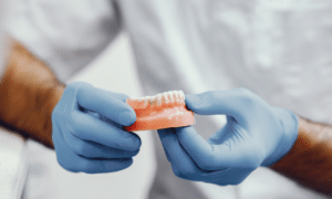 Dentist holding dental prosthetic model wearing blue gloves for patient education.