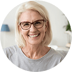Smiling female dentist wearing glasses and light blue scrubs in dental office.