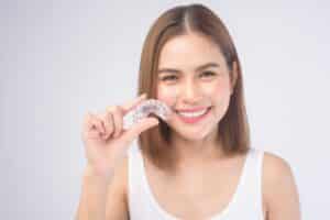 Smiling woman holding clear Invisalign aligner tray for teeth straightening treatment.