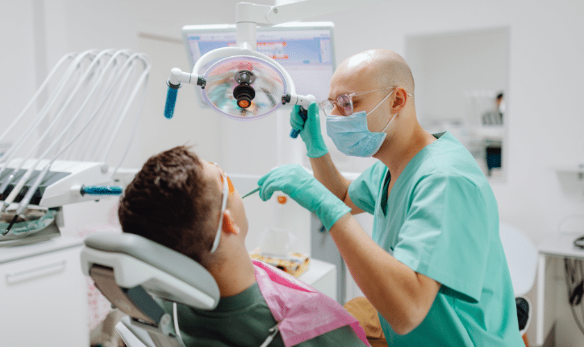 Dentist examining young patient's teeth under overhead light in modern dental office.