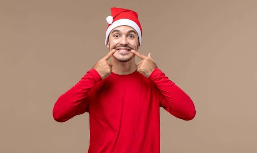 Man in Santa hat pointing to his smile, promoting holiday dental health.