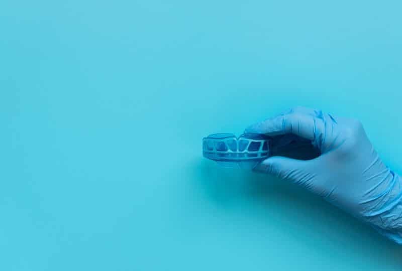 Gloved hand holding a dental model on blue background.