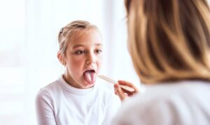 Young girl sticking out tongue for dental examination by healthcare provider.
