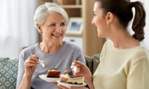 Older woman and younger woman enjoying dessert together while smiling during Mother's Day celebration.