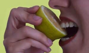 Person biting into a lemon wedge against a yellow background to illustrate vitamin C benefits for dental health.