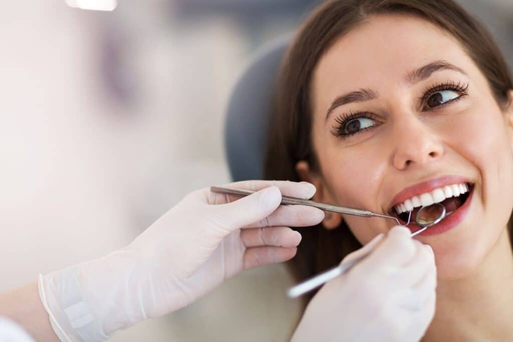 Woman receiving dental examination with mirror and explorer tool during smile evaluation.