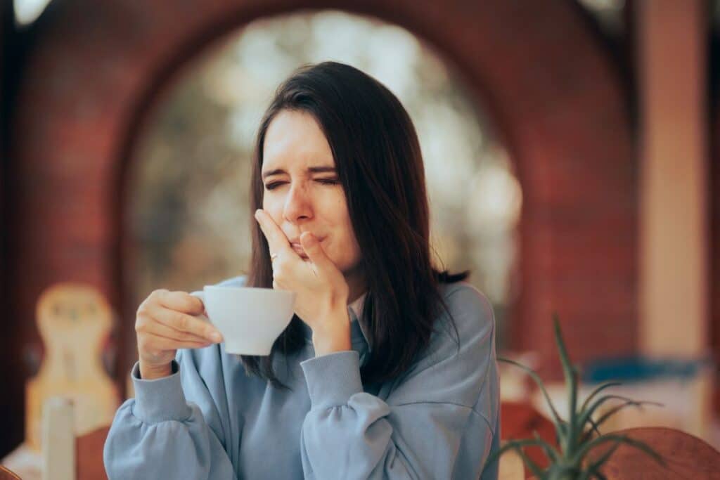 Woman experiencing tooth sensitivity while holding a cup after dental whitening treatment.