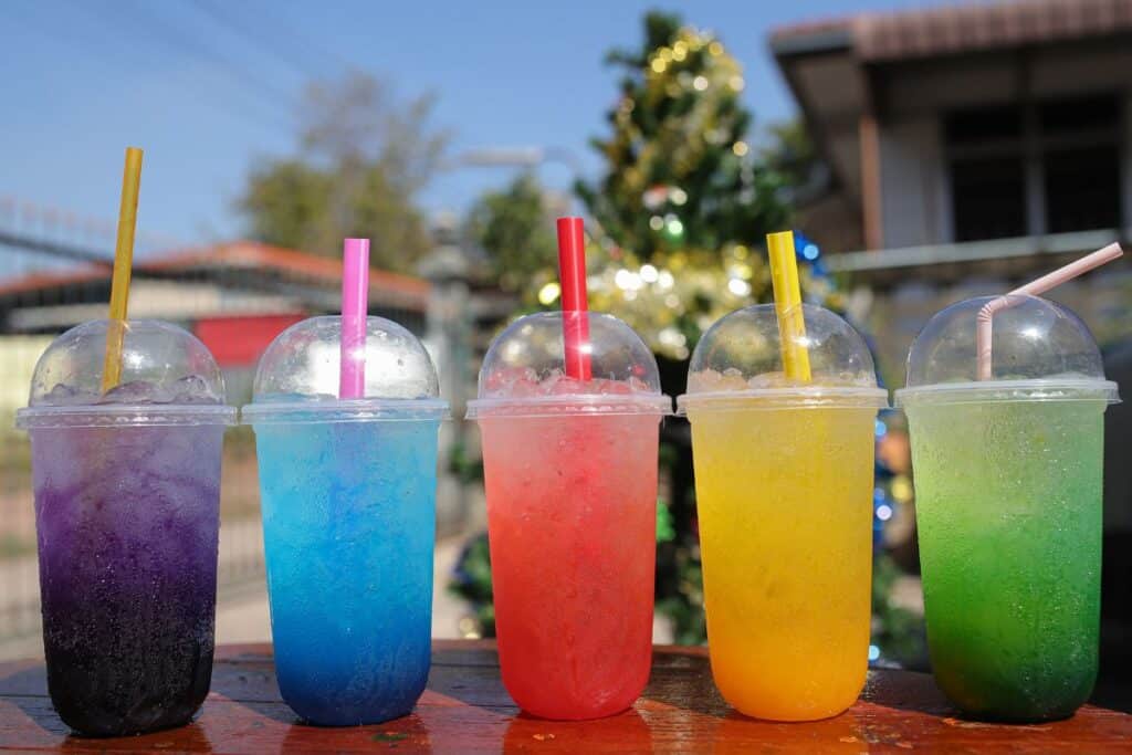 Five colorful flavored beverages in clear cups with straws, illustrating drinks that may harm dental health.