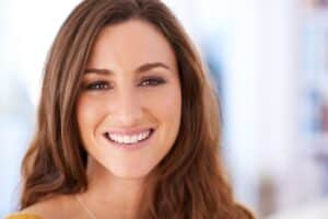 Woman smiling brightly with healthy white teeth in dental office setting.