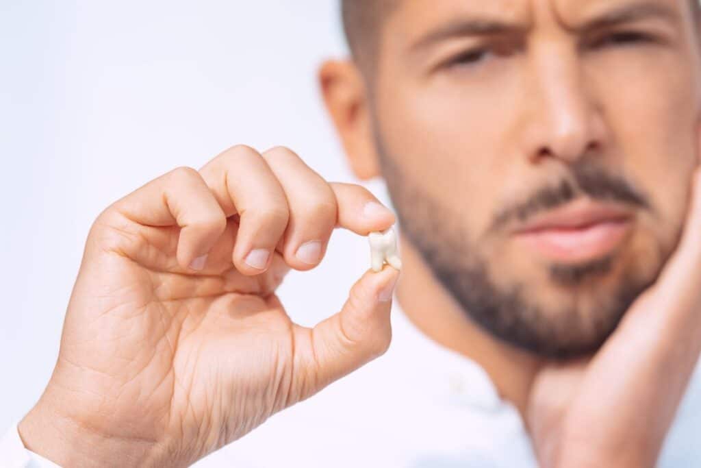 Man holding a cracked tooth, wincing in pain from potential gum disease complications.