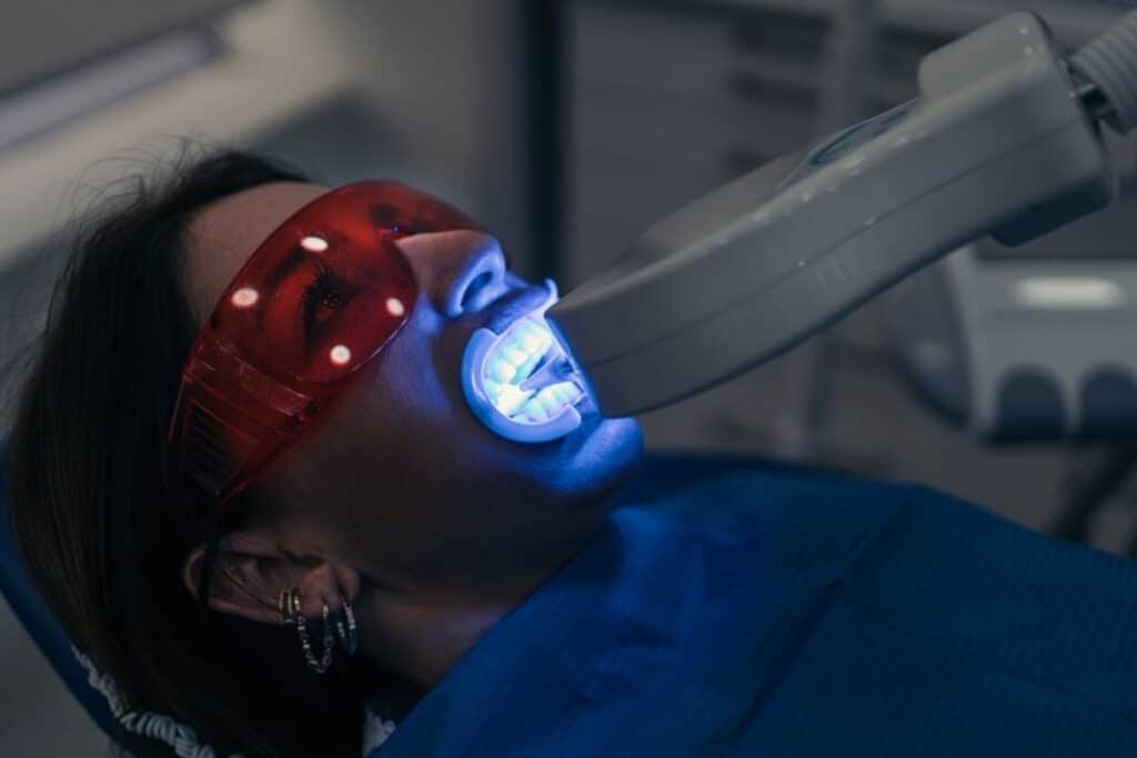 Patient receiving professional teeth whitening treatment with blue LED light activation.