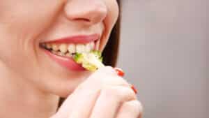 Woman smiling while eating fresh broccoli, demonstrating healthy eating habits for dental health.