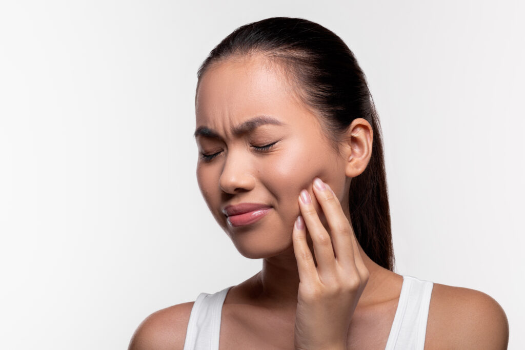 Woman experiencing jaw pain, touching her cheek with a concerned expression.