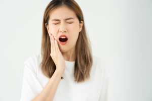 Woman experiencing tooth sensitivity pain, holding her cheek and grimacing.