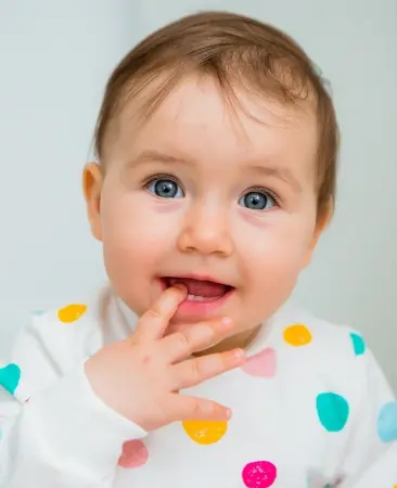 Smiling toddler with colorful polka dot shirt, showing healthy baby teeth and happy expression.