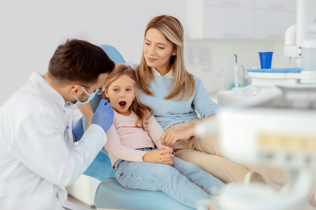 Young girl in dental chair with mother present during pediatric dental examination and checkup.