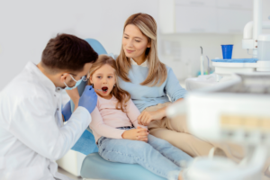 Young girl in dental chair with mother present during pediatric dental examination and checkup.