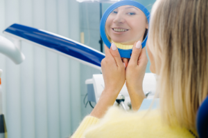 Woman smiling at mirror during nighttime oral care routine in dental office.