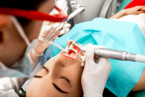 Dentist performing professional cleaning on patient's teeth with dental tools and suction.