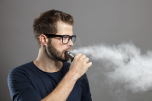 Man vaping with large cloud of vapor exhaled, illustrating oral health risks from e-cigarettes.