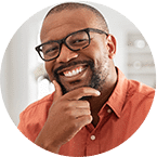 Smiling male dentist wearing glasses and orange shirt in professional headshot.
